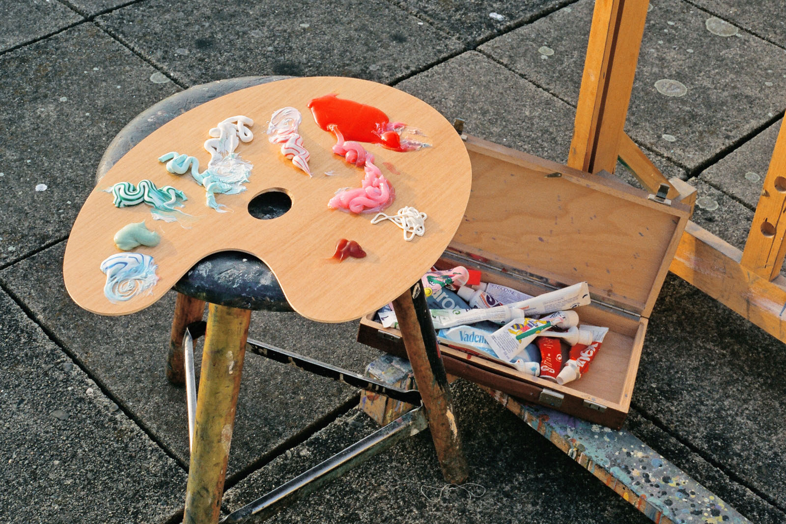 Kunst-Installation von Josephine Riemann (Detail): Künstlerpalette, die mit Farbklecksen von verschiedenen Zahncremes bedeckt ist. Im Hintergrund ist eine Staffelei und ein Malkasten mit Zahnpastatuben aufgebaut. 