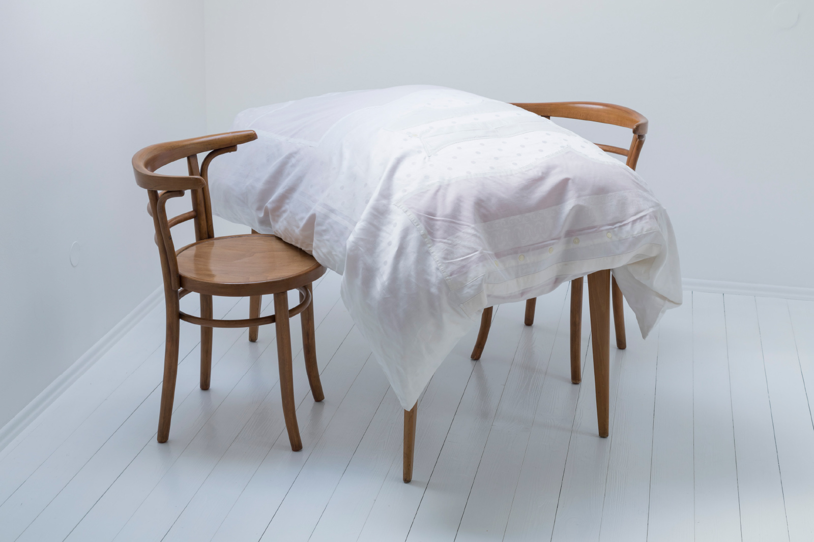 Kunst-Installation von Josephine Riemann: Ein zerlegtes Herrenoberhemd ist in eine Tischdecke eingenäht worden. Diese wurde mit einem Federbett unterlegt und auf einem Tisch präsentiert.