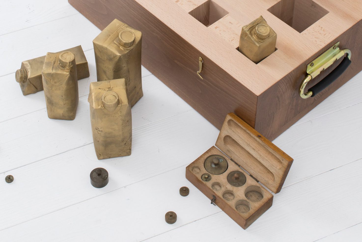 Objekte von Josephine Riemann (Detail): 8 Tetrapak-Verpackungen unterschiedlicher Größe, in Messing abgegossen in einem Vollholzkasten.  