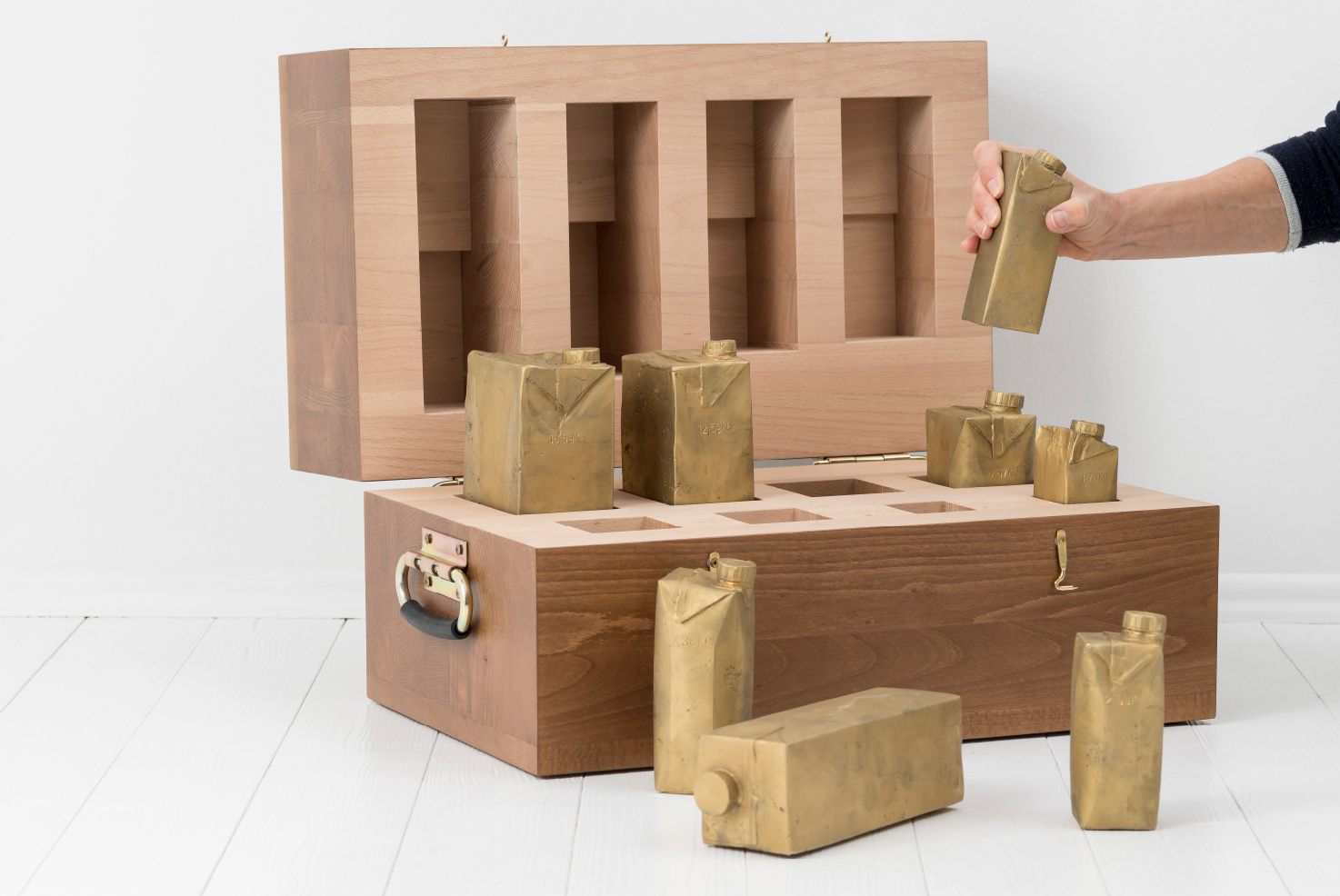 Objekte von Josephine Riemann: 8 Tetrapak-Verpackungen unterschiedlicher Größe, in Messing abgegossen in einem Vollholzkasten.